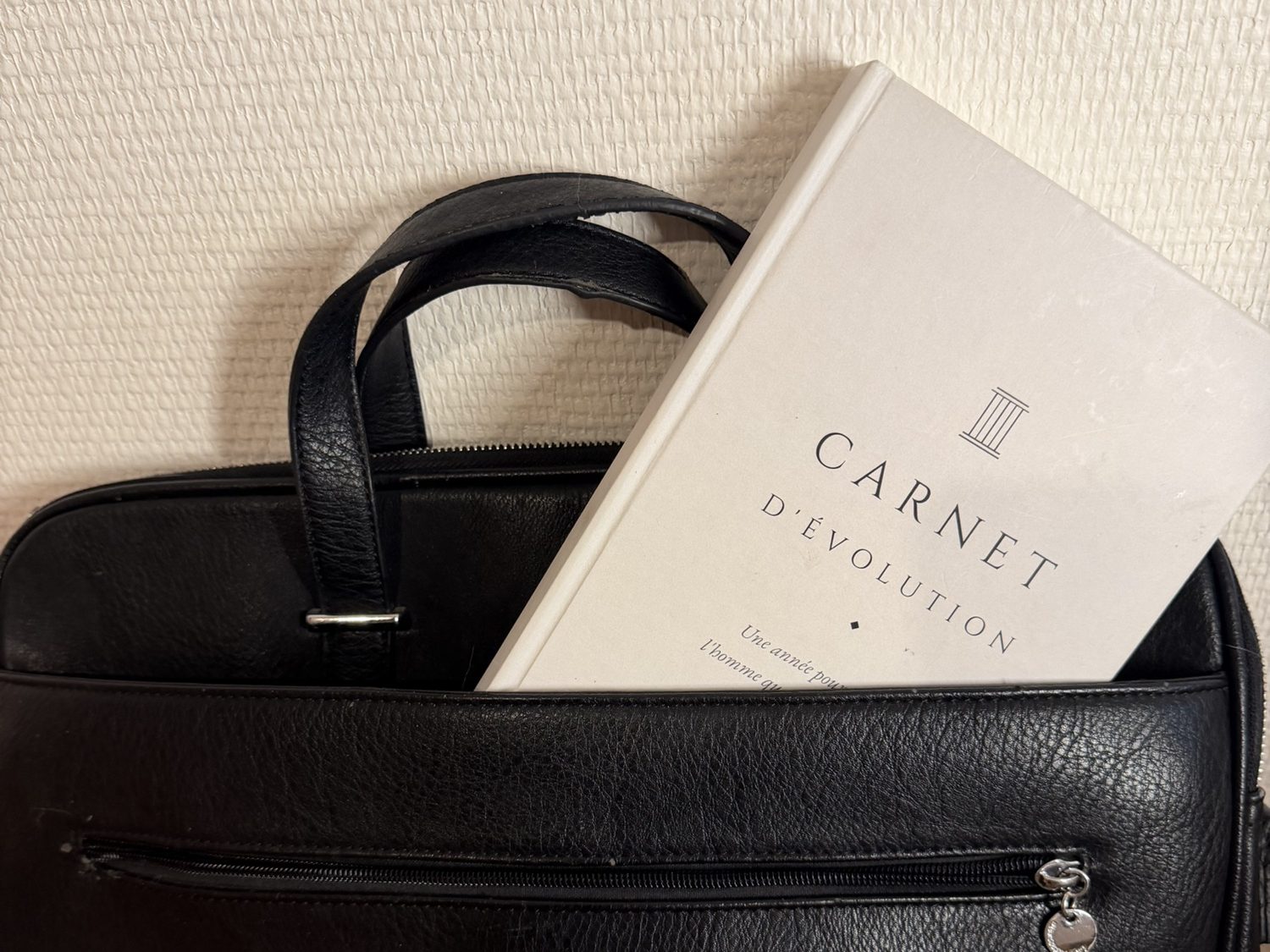 Le Carnet d'évolution glissé dans un sac en cuir noir